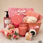Pink gift basket with soap, candle, bath items, towels, and a small flower bouquet