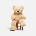 Large beige teddy bear sitting on a small wooden stool