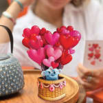 Heart-shaped balloon bouquet in a small basket with a teddy bear