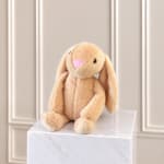 Plush beige bunny with long ears sitting on a white pedestal