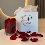 Red rose petals in a glass container beside a floral gift box