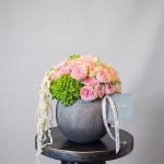 Pink roses and green hydrangea in a dark round vase with trailing white flowers