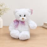 White teddy bear with a pink plaid bow sitting on a wooden surface