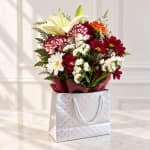 Mixed bouquet with lilies, daisies, carnations, and roses in a gift bag