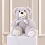 Gray teddy bear with a white ribbon sitting on a white pedestal
