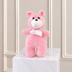 Pink crocheted teddy bear standing on a marble pedestal