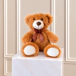 Brown teddy bear with a ribbon sitting on a white pedestal