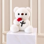 White teddy bear holding a red rose on a marble pedestal