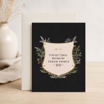Black greeting card with a motivational quote and floral border, leaning against an envelope