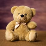 Plush teddy bear with a satin bow sitting on a brown surface
