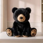 Black teddy bear plush sitting on a white surface