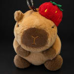 Plush teddy bear keychain with a red strawberry hat on a black background