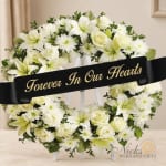 White floral funeral wreath with a black memorial ribbon on a stand
