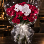 Red carnation bouquet with white orchids wrapped in clear cellophane and a white bow