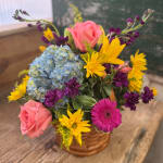 Mixed bouquet in a woven basket with pink roses, blue hydrangea, and yellow daisies