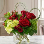Red roses and green hydrangeas in a clear glass vase with heart-shaped loops