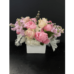 Low arrangement of pink peonies and blush roses in a white square vase with soft white flowers.