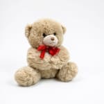 Beige teddy bear with a red ribbon bow on a white background