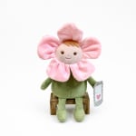 Plush flower-shaped doll with pink petals and a small card, seated on a wooden stool