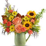 Mixed bouquet of roses, sunflowers, and daisies in a green pitcher vase