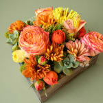 Orange and pink floral arrangement in a wooden box with succulents