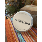 A tin candle labeled cactus flower sits on a woven textile.