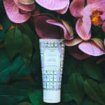 Lavender hand cream tube surrounded by pink orchid blooms and dark green leaves