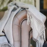A light gray throw blanket draped over a beige upholstered chair