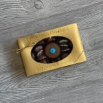 Gold box of assorted chocolates with a clear window showing a round piece topped with a blue flower design