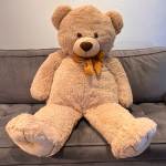 Large tan teddy bear with a bow sitting on a gray couch