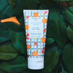 Tube of Beekman 1802 Juicy Peachy Lychee hand cream on dark green leaves