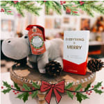 Plush hippo with a Christmas tag beside a shower steamer box on a wooden tray