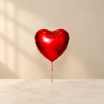 Red heart-shaped balloon on a string against a plain background
