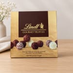 Box of Lindt gourmet truffles on a table with a vase of white flowers in the background