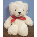 White plush teddy bear with a red bow sitting on a tabletop against a blue background