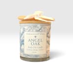A labeled candle jar with a wooden lid and ribbon bow