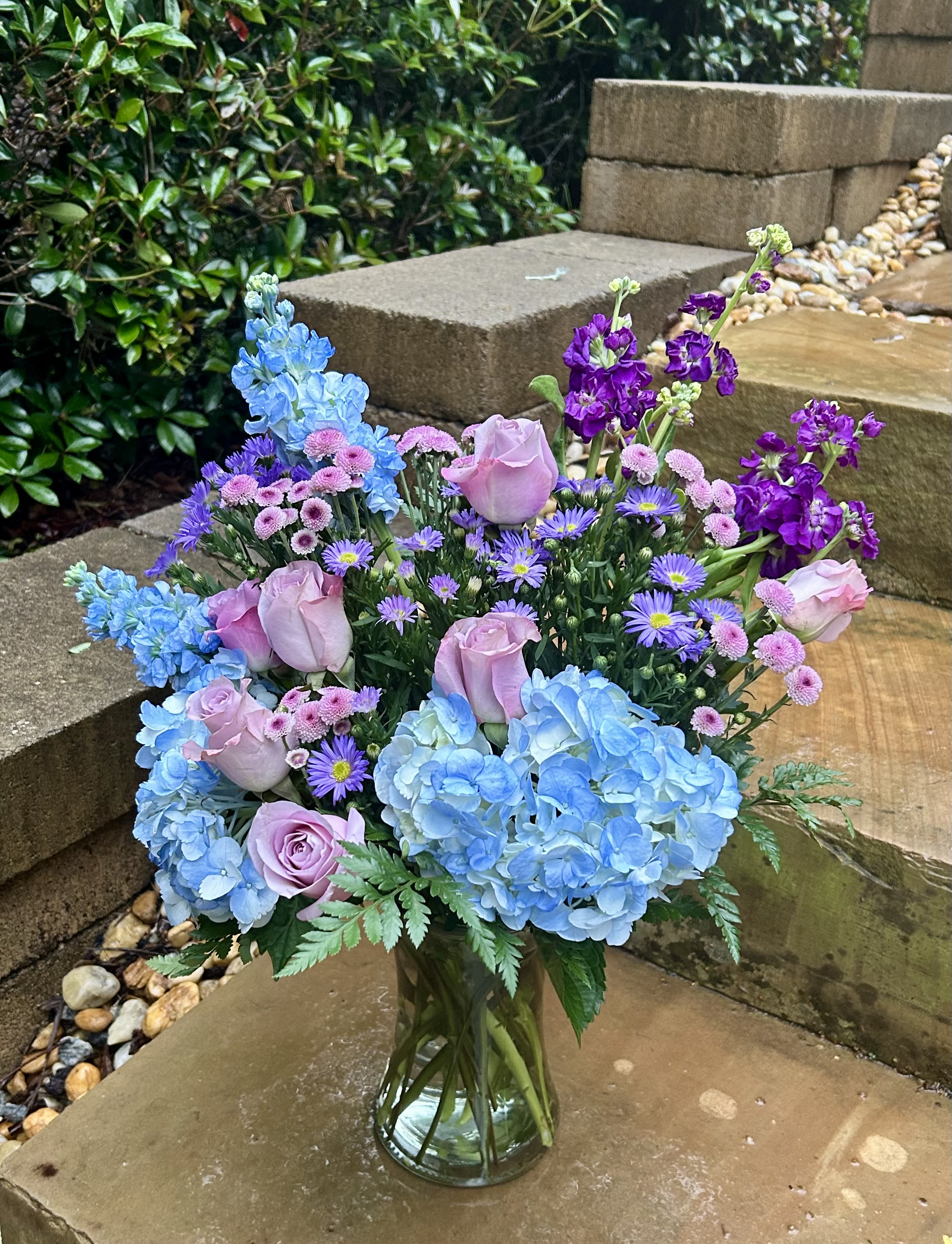 Bouquet of blue hydrangeas, pink roses, and purple flowers in a glass vase