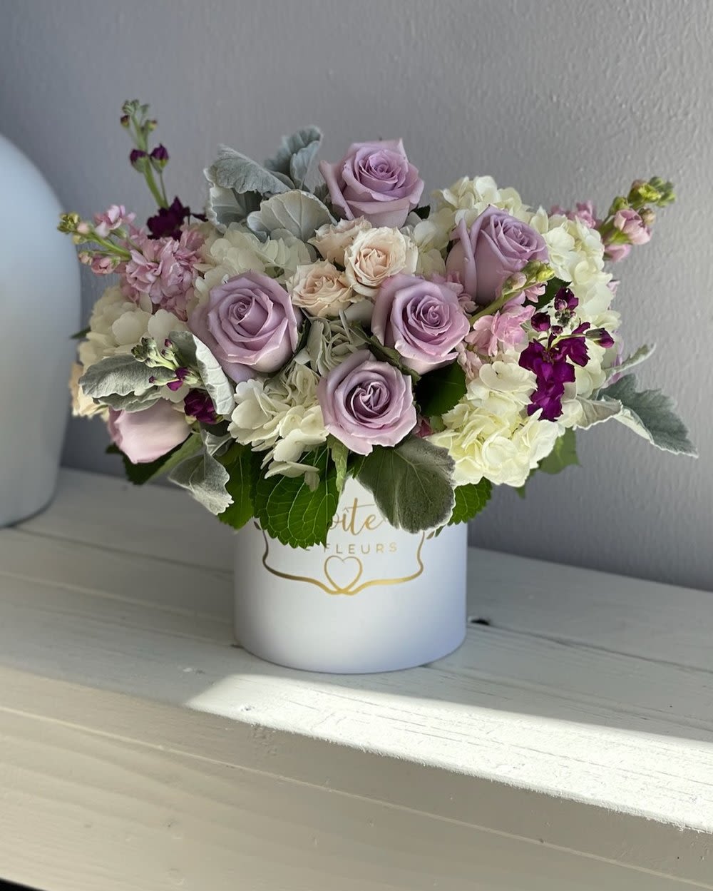 Lavender roses and white hydrangeas in a white hatbox