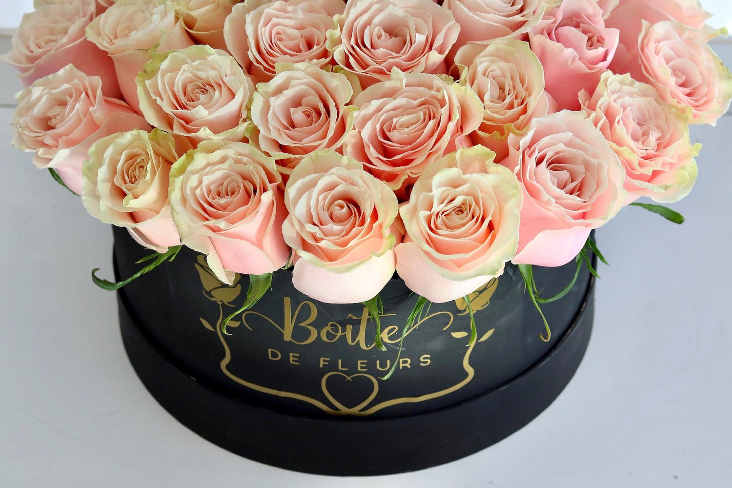 Pink roses arranged in a black round box with gold lettering