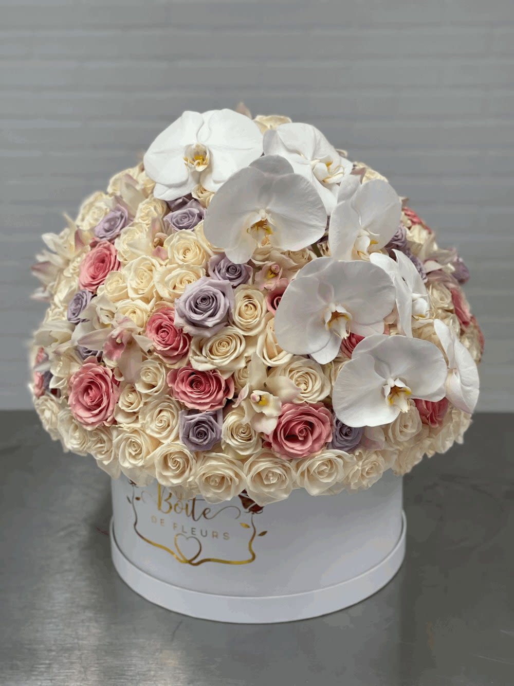 Round bouquet of white orchids and pastel roses in a white hat box