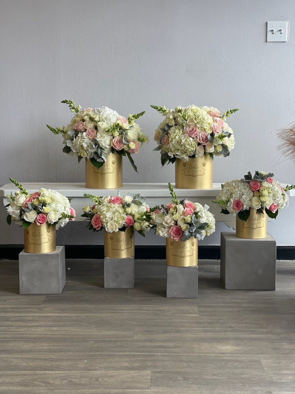 Five pastel floral arrangements in gold cylinders on gray pedestals