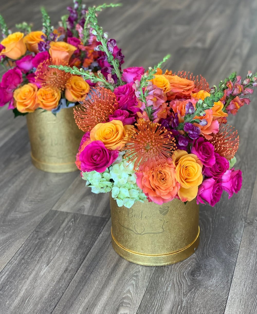 Two colorful floral arrangements in gold round containers