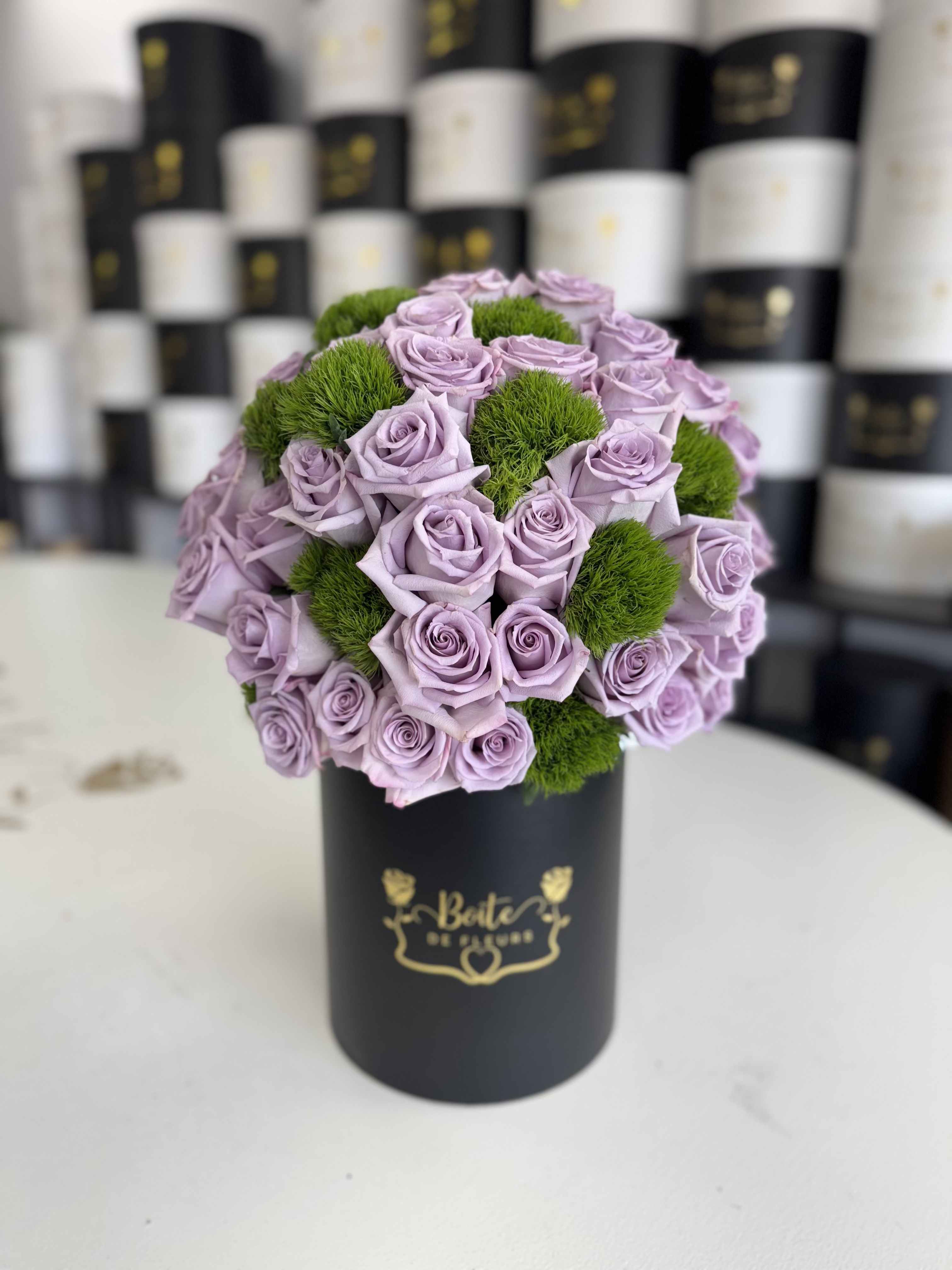 Lavender roses arranged with green pom-pom accents in a black hat box