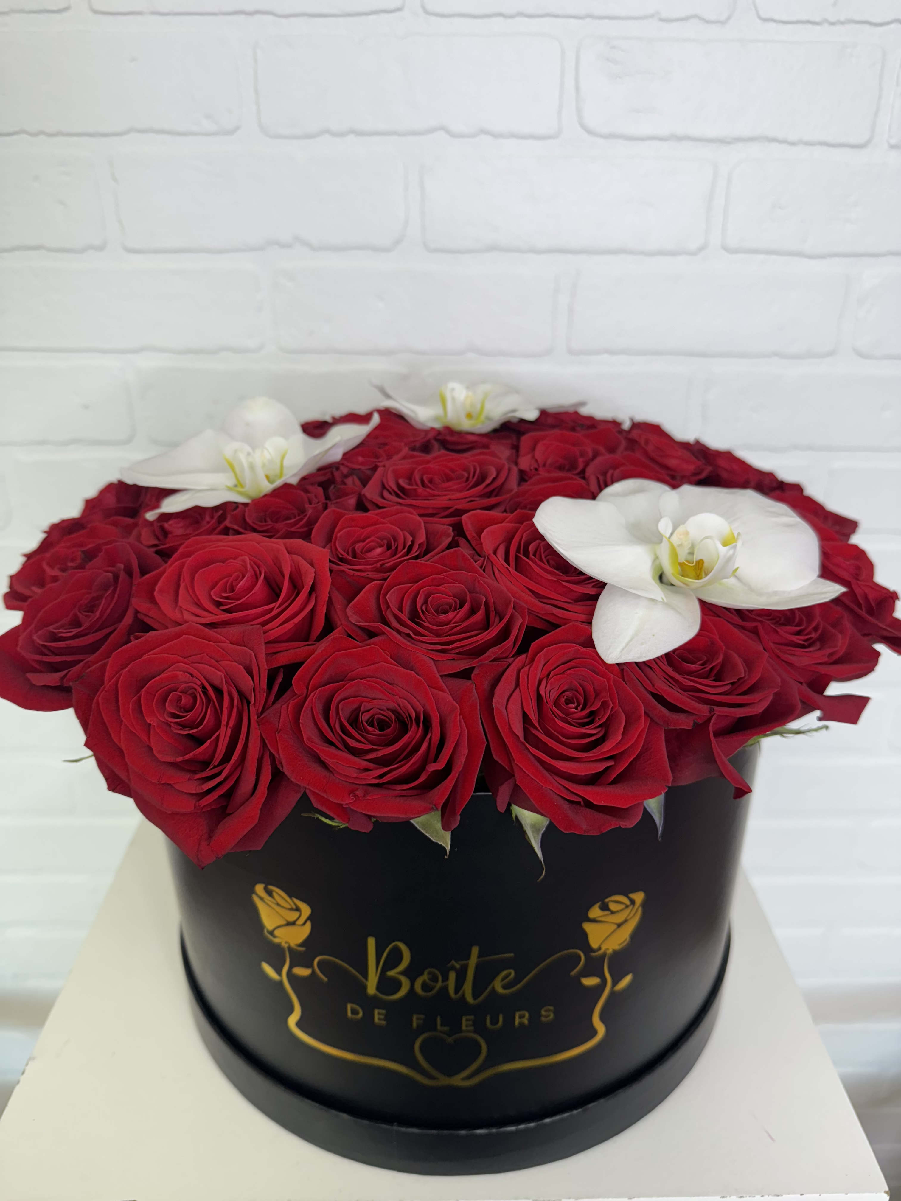 Red roses and white orchids arranged in a black round box