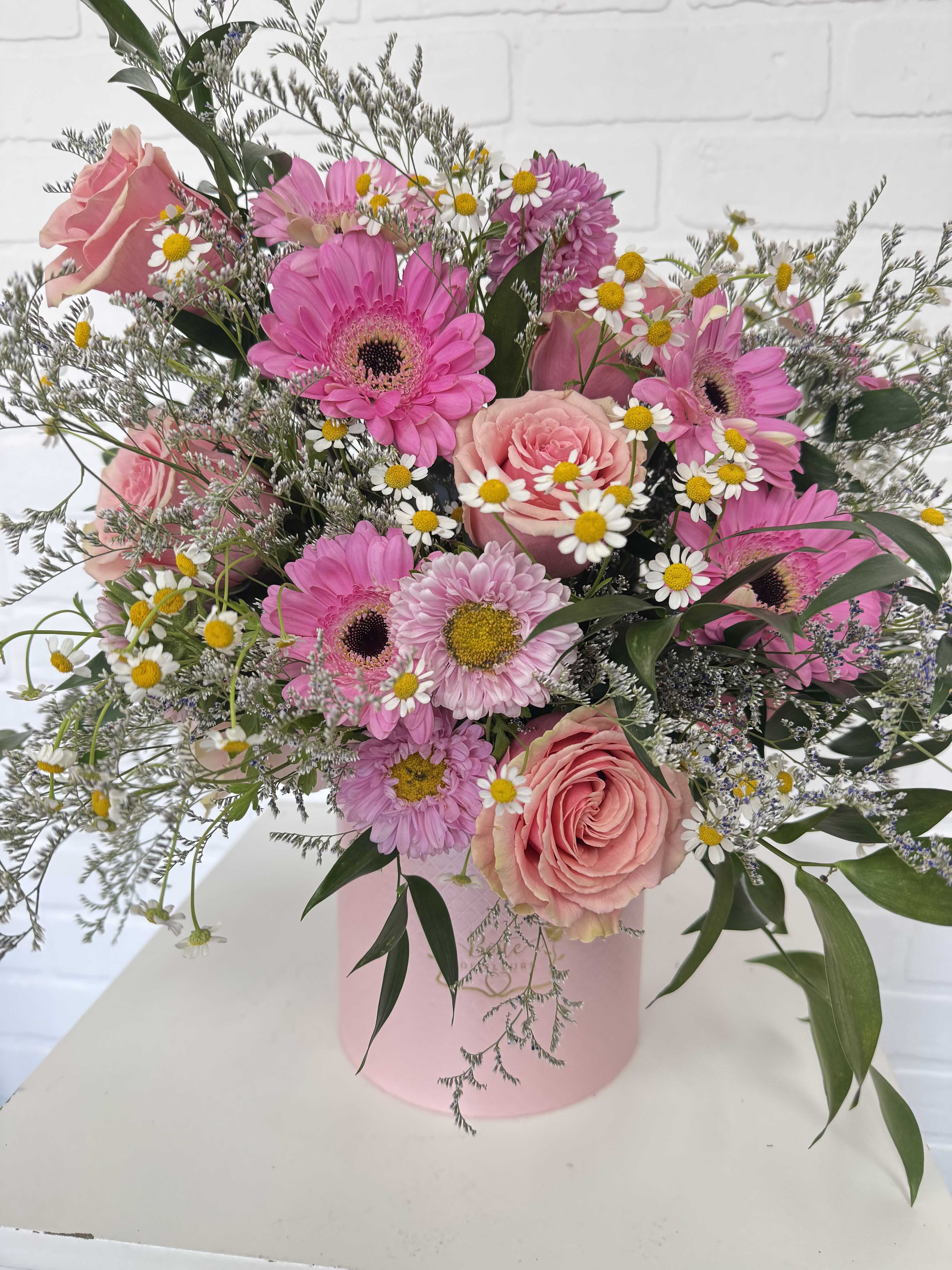 Pink roses and gerbera daisies in a pink hatbox with small white daisies