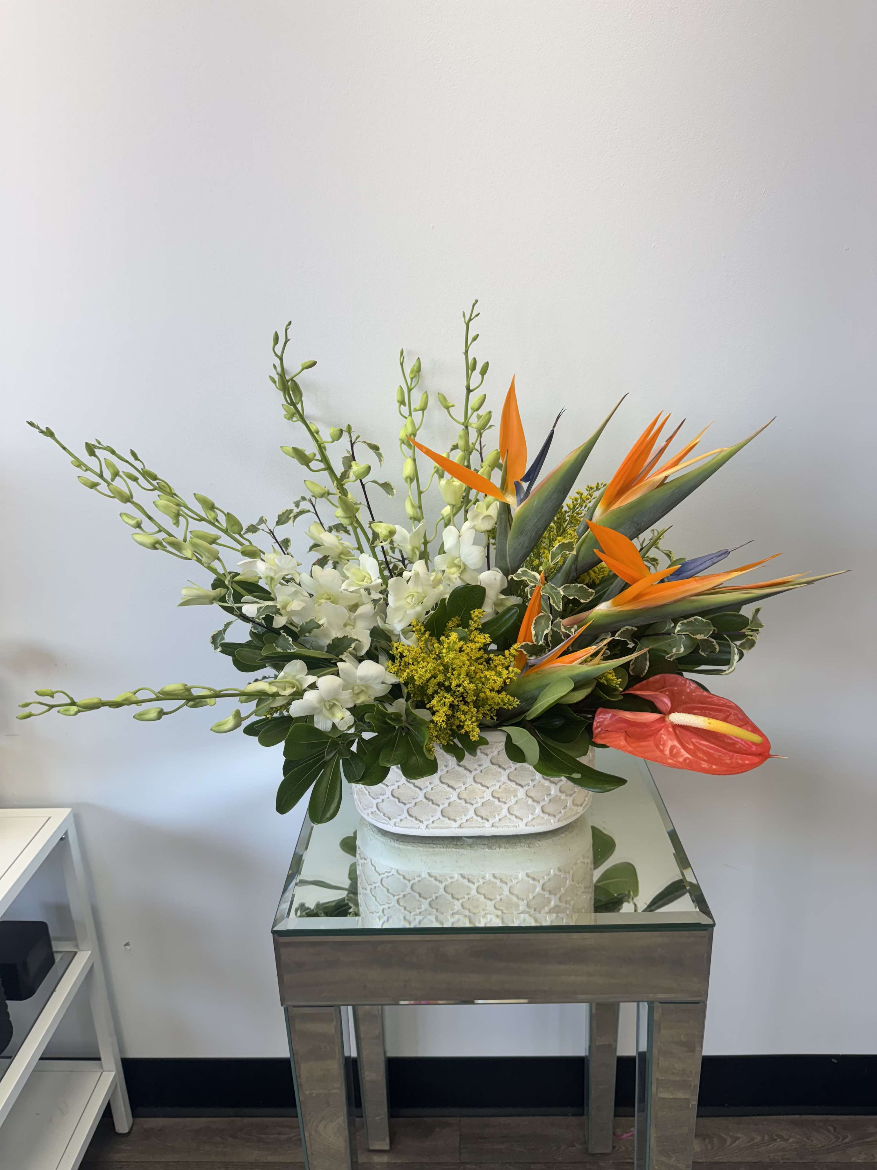 Tropical floral arrangement with white orchids and orange bird-of-paradise in a white vase