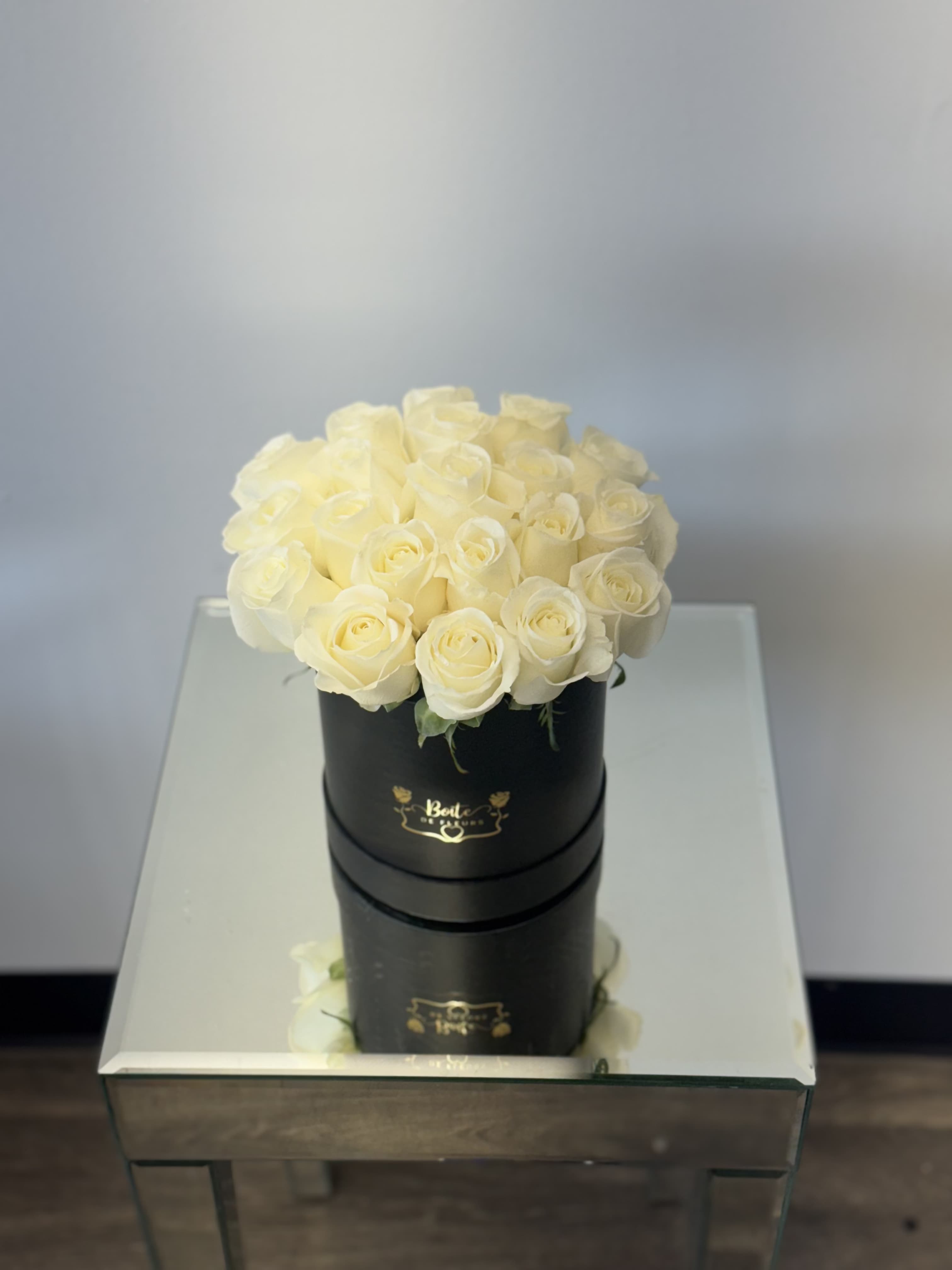 Cream roses arranged in a black round box on a mirrored table