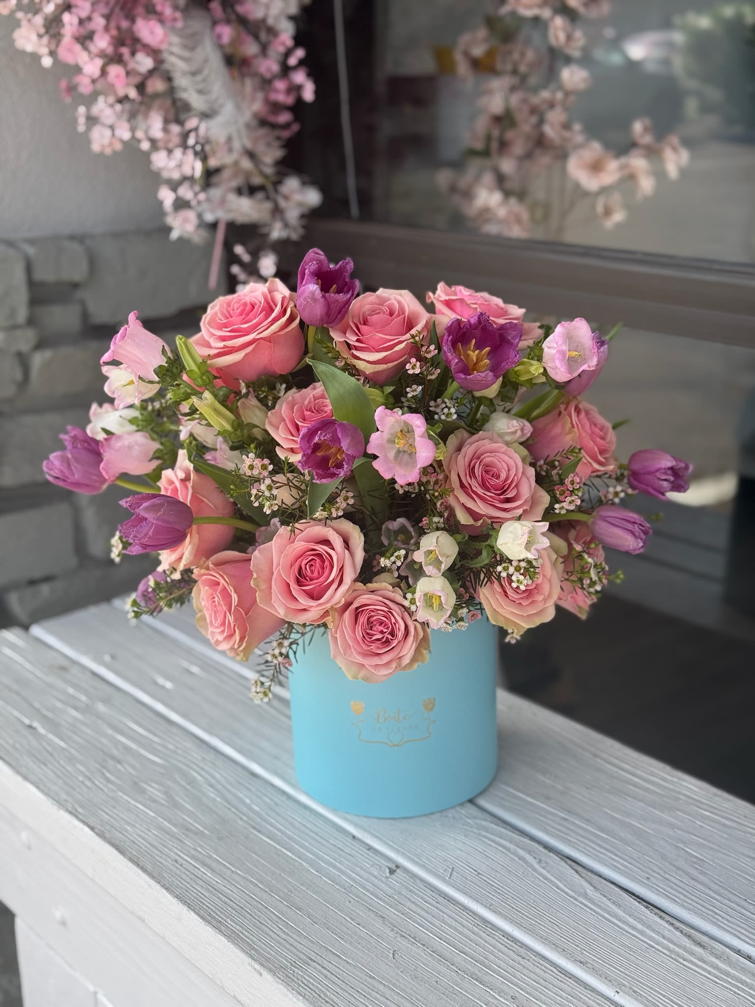 Pink roses and purple tulips arranged in a blue hat box