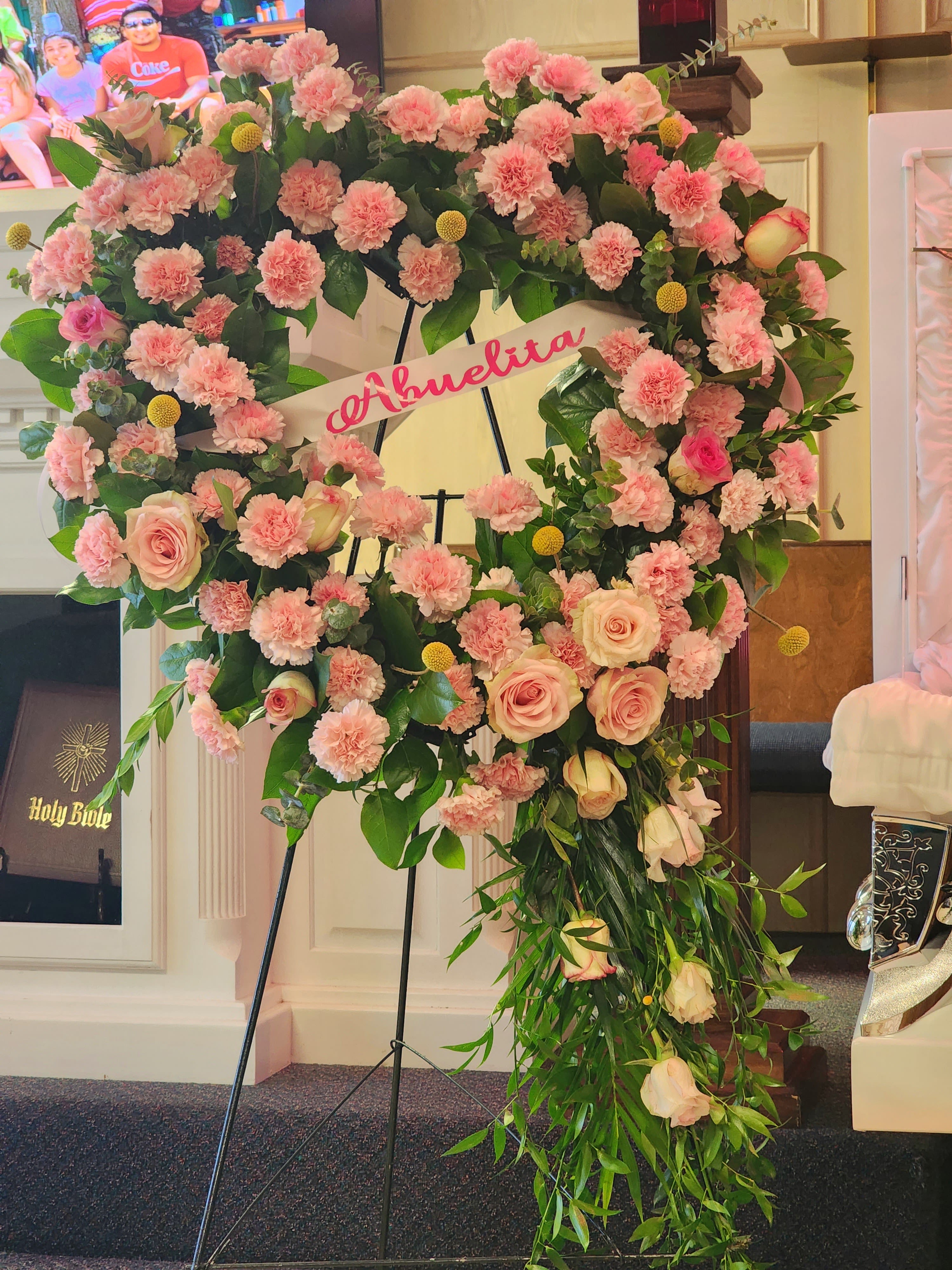 Large pink floral wreath on a stand with a name ribbon