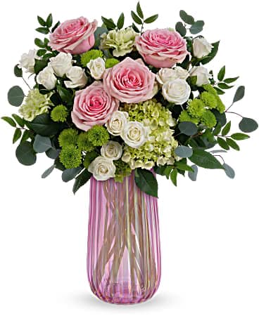 Pink and white rose arrangement with green accents in a tall ribbed pink glass vase
